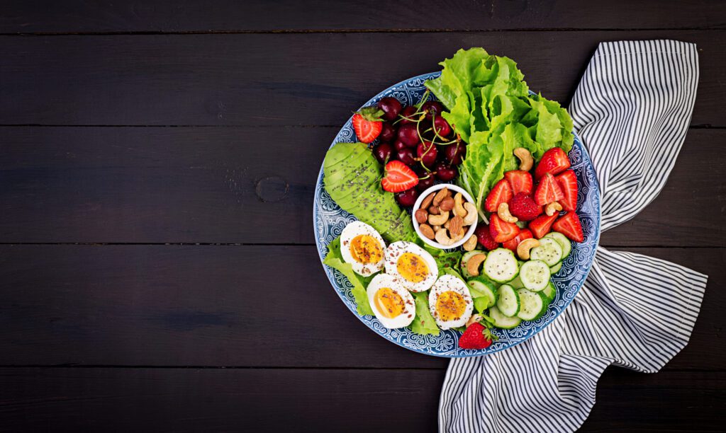plate with paleo diet food boiled eggs avocado cucumber nuts cherry strawberries paleo breakfast top view scaled 2